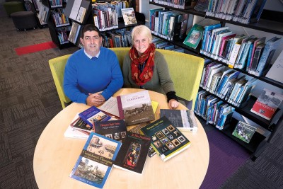 Hamish Faulls and Mary Leota in the College library with a table of books which are to be used as part of the new curriculum.