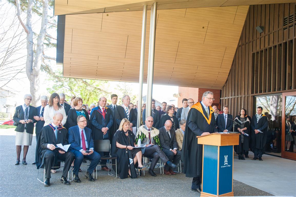 The official party seated behind a guest speaking outside the front of the Centennial Chapel during the Dedication event