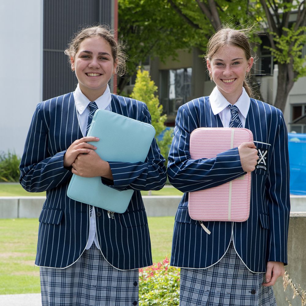 Two smiling boarding students outside the boarding houses holding their laptops.