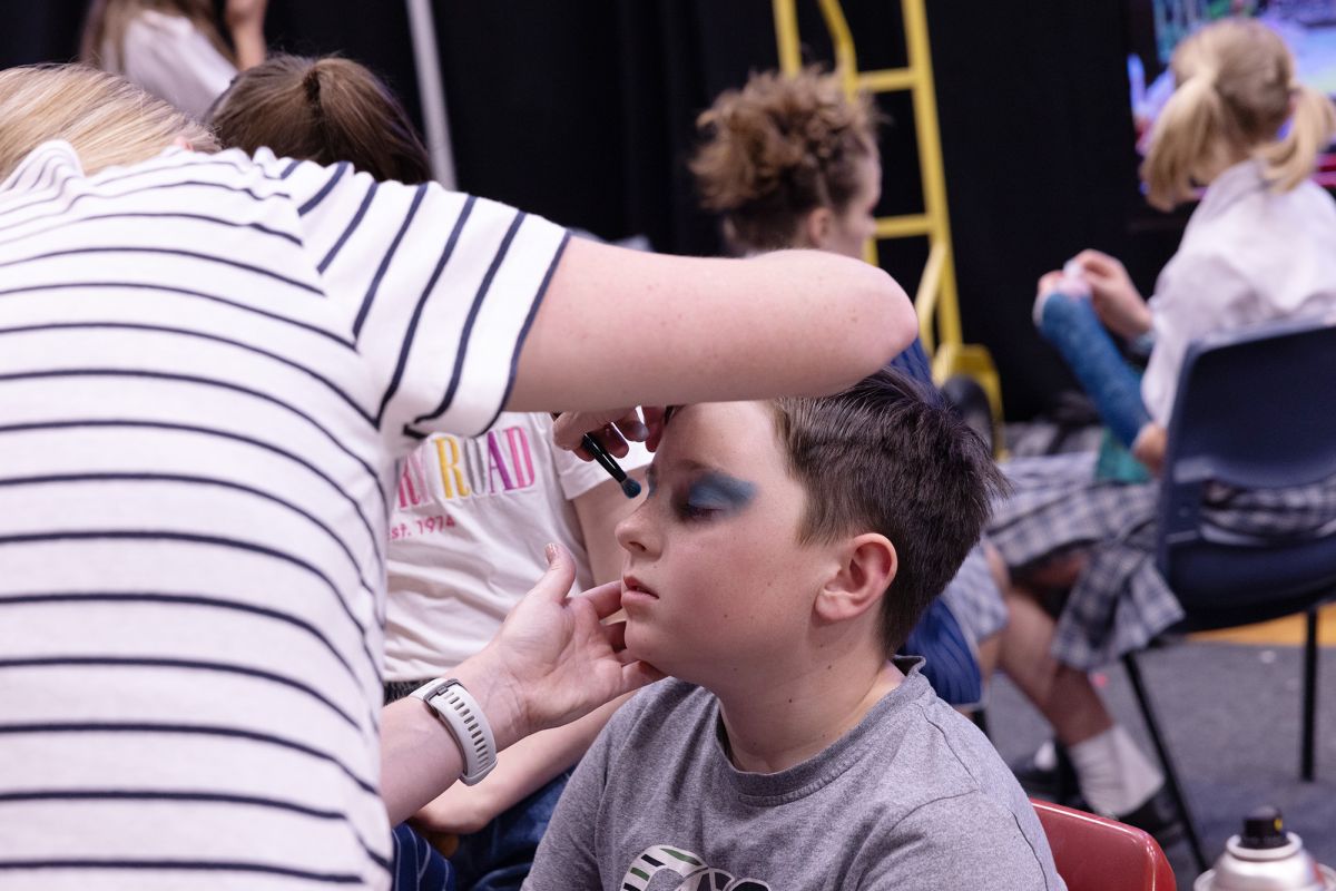 A volunteer putting makeup on a student for production.