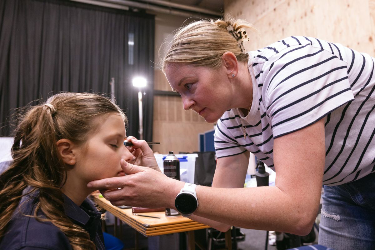 A volunteer putting makeup on a student for production.