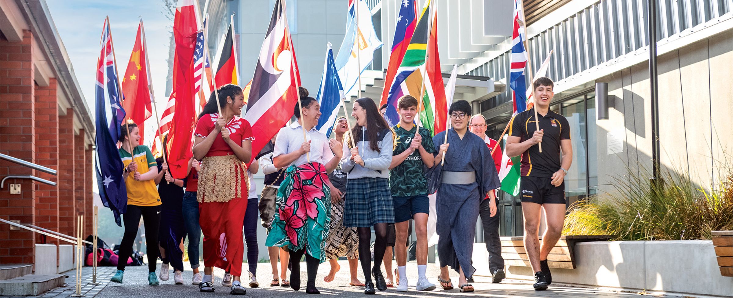 St Andrew's College international students in national dress with flags walking through the campus