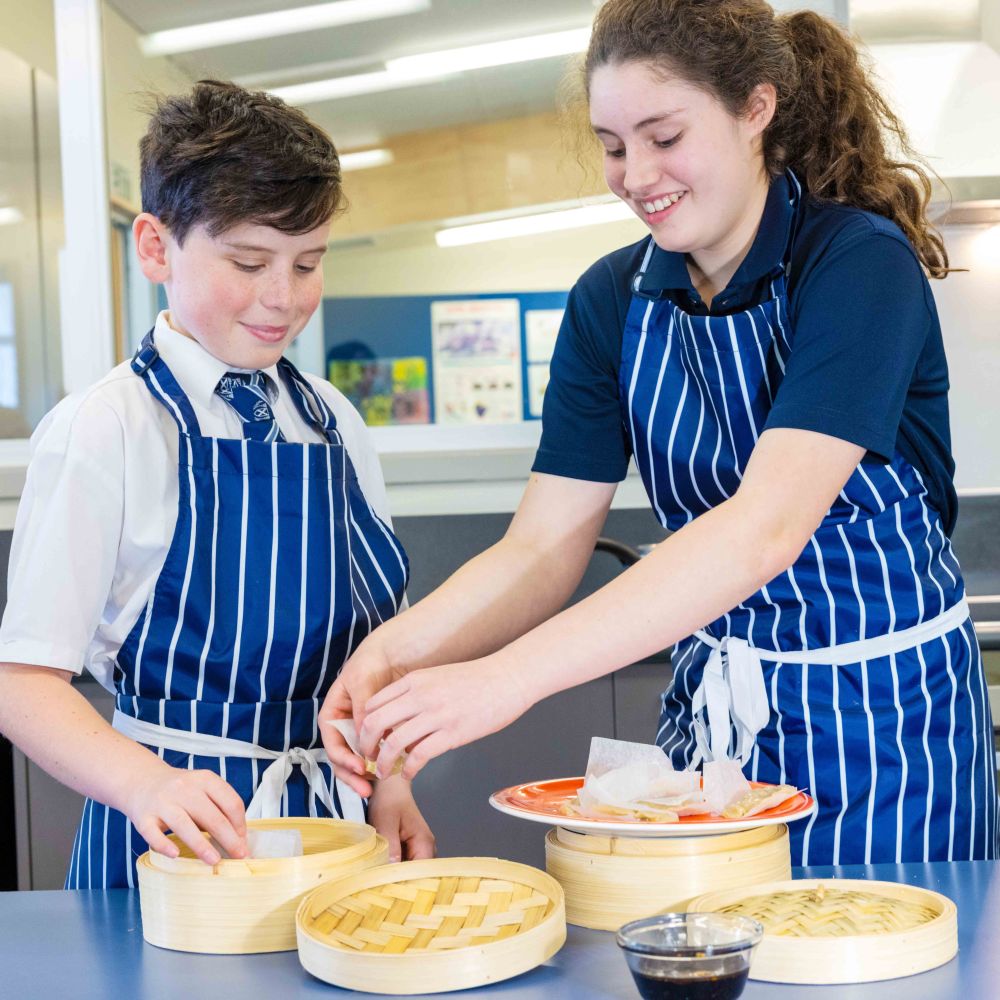 Two students steaming dumplings in food class wearing aprons