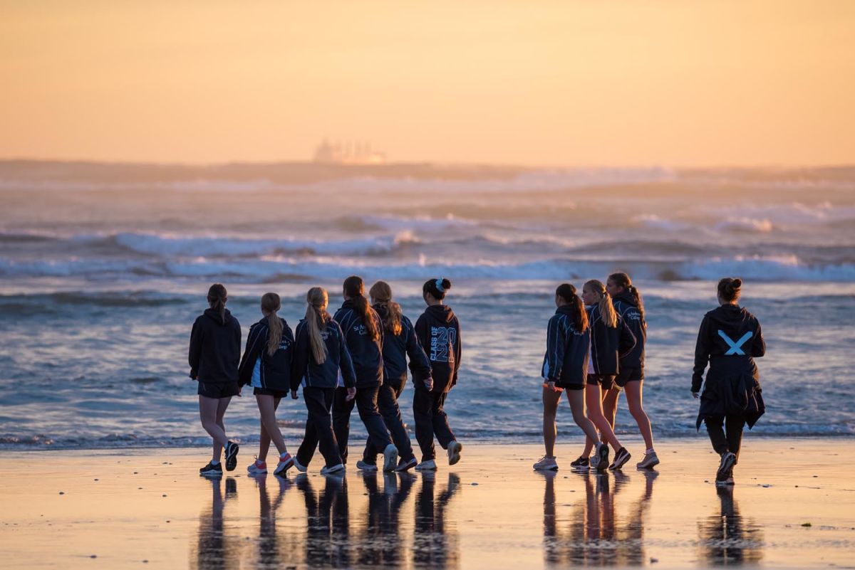 Group of students in PE gear walking along the sea shore as the sun comes up.