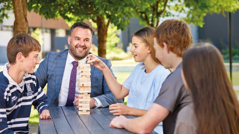 Boarding Director with students outside at table playing Jenga