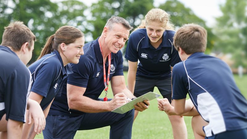 Sports teacher with students in PE uniform looking at game plan