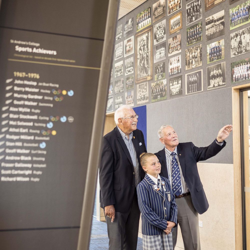 Old Collegians and preparatory school student looking at sports wall display